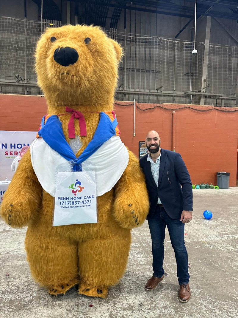 Team member with the Penn Home Care bear mascot at an indoor event